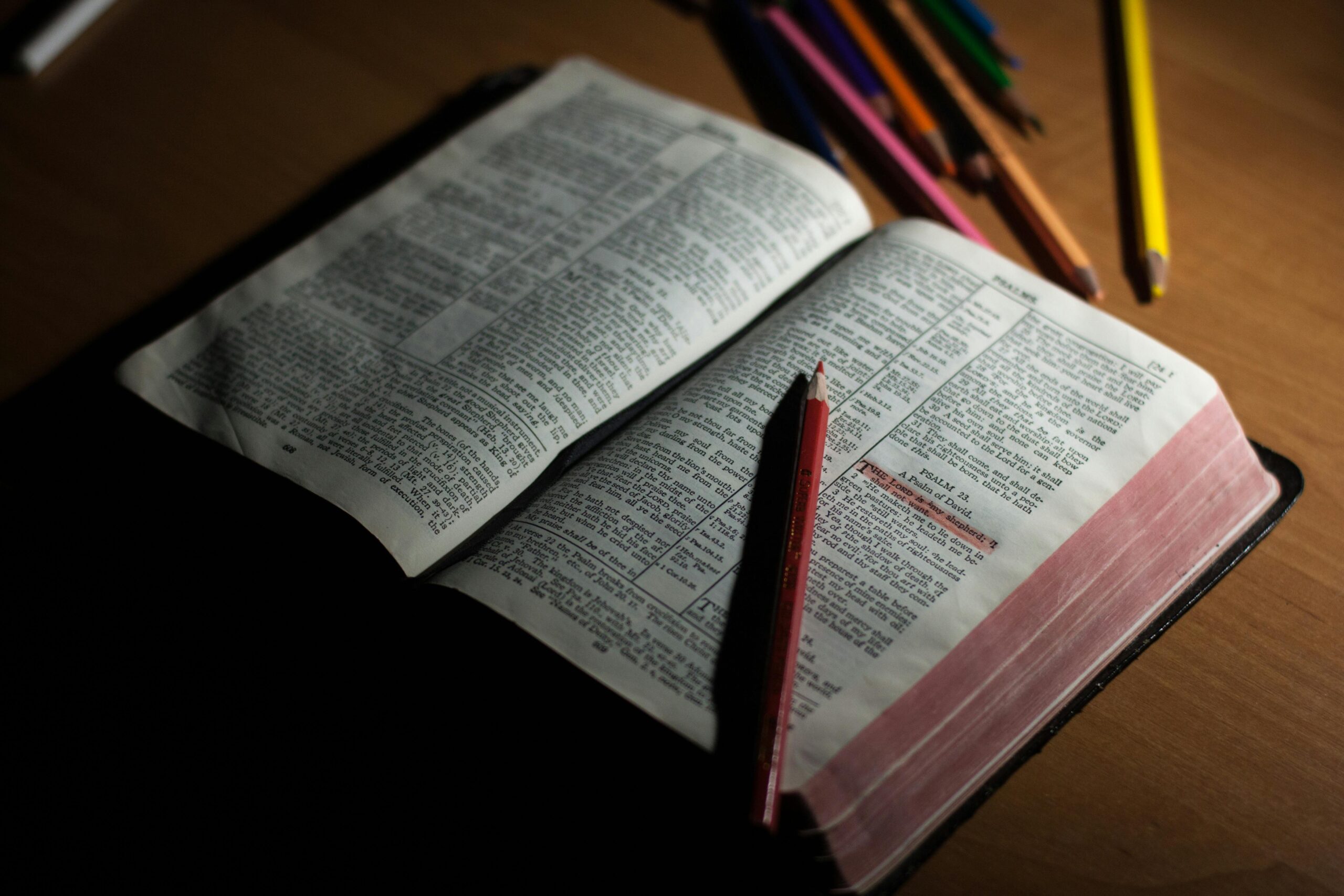 An open Bible on a wooden table accompanied by colored pencils, symbolizing study and spirituality.